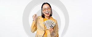 Microcredit and money concept. Stylish asian young woman in sunglasses, laughing happy, holding dollars cash, standing