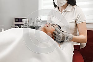 Microcurrent therapy. Cosmelotologist makes stimulating facial massage with electric gloves. Lymphatic drainage massage