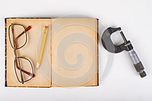 Micrometer and old book with glasses on a white table. Workshop accessories