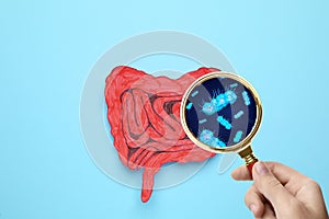 Microorganisms research. Woman with magnifying glass and paper intestine cutout on light blue, top view