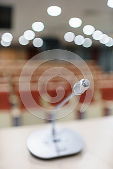 Microphone in the foreground. Seminar presentation. Conference room full of empty seats. Red color. Hall for workshops