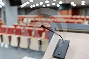 Microphone in the foreground. Seminar presentation. Conference room full of empty seats. Red color. Hall for workshops