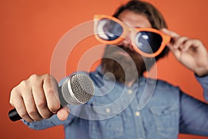 microphone in hand of caucasian hipster with beard and stylish hair in arty glasses, selective focus, device