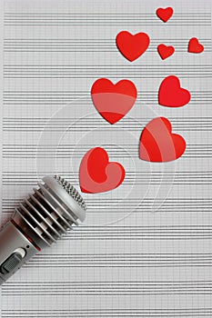 Microphone and paper red hearts are located on a clean music notebook. The concept of music and love. Valentine`s day