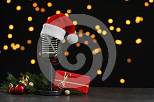 Microphone with Santa hat and decorations on table against blurred lights, space for text. Christmas music