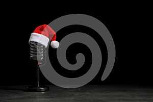 Microphone with Santa hat on grey stone table against black background. Christmas music