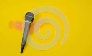 Microphone with soft light pink feathers in the shape of wings on a yellow background. Text space. Podcast, creative concept.