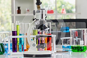 Microscopes place in the laboratory with red, orange, blue chemicals in the beaker and tube