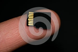 Microsd card on human finger over black background,hi tech data storage devices