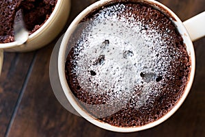 Microwave Brownie Chocolate Mug Cake with Powder Sugar on Dark Wooden Surface.