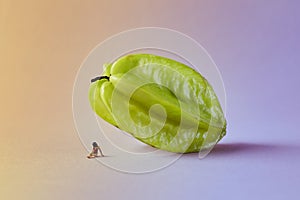 Microworld with woman figure under the carambola tropical fruit on green pink background. Cartoon style, food photography. photo