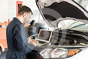 Worker Using Laptop To Detect Malfunction In Car At Garage photo