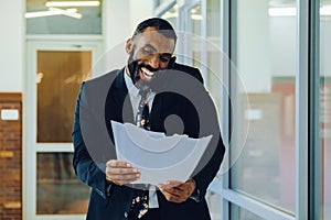 Mid adult bearded black man Entrepreneur Businessman wearing suit holding papers and talking on smartphone laughing