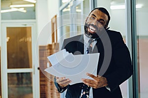Mid adult bearded black man Entrepreneur Businessman wearing suit holding papers and talking on smartphone laughing