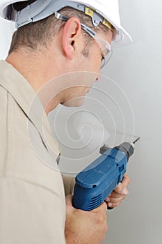 mid-adult builder man drilling hole in wall