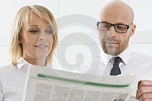 Mid adult business couple reading newspaper in kitchen