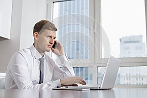 Mid adult businessman on call while using laptop at home