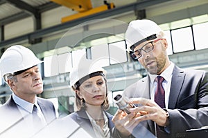 Mid adult businessman explaining machine part of colleagues in metal industry