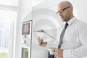 Mid adult businessman having coffee while reading newspaper at home