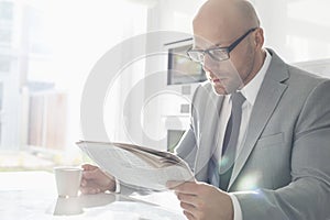 Mid adult businessman having coffee while reading newspaper at home