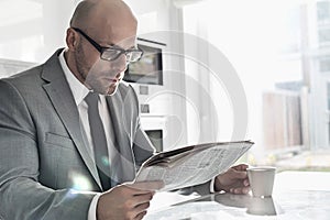 Mid adult businessman having coffee while reading newspaper at home