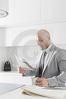 Mid adult businessman having coffee while reading newspaper in kitchen