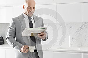 Mid adult businessman having coffee while reading newspaper in kitchen