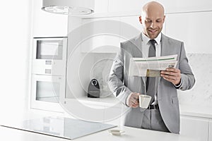 Mid adult businessman having coffee while reading newspaper in kitchen