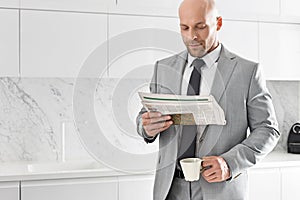 Mid adult businessman having coffee while reading newspaper in kitchen