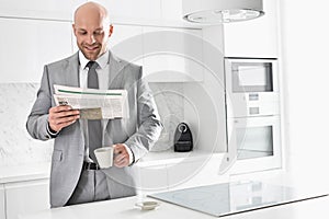 Mid adult businessman having coffee while reading newspaper in kitchen