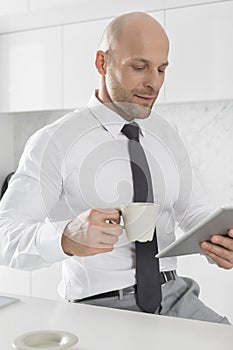 Mid adult businessman having coffee while using tablet PC in kitchen