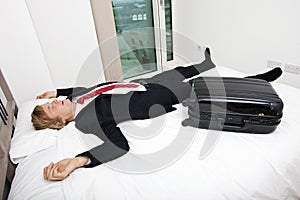 Mid adult businessman with luggage sleeping in bed at home