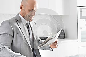 Mid adult businessman reading newspaper in kitchen