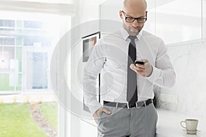 Mid adult businessman text messaging through smart phone at home