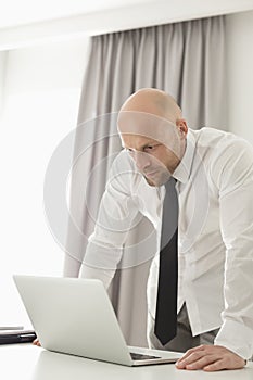 Mid adult businessman using laptop at table in home office