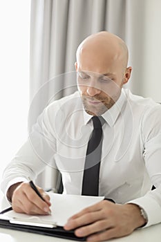 Mid adult businessman writing on clipboard in home office