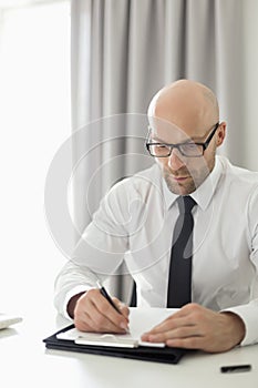 Mid adult businessman writing on clipboard in home office