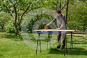 Mid adult caucasian man in the garden sanding wooden planks. DIY home improvement, restoration, carpentry concept.