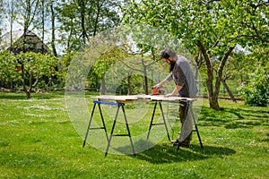 Mid adult caucasian man in the garden sanding wooden planks. DIY home improvement, restoration, carpentry concept.