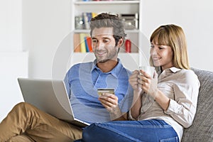 Mid adult couple shopping using laptop and credit card in modern apartment