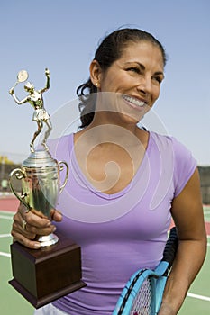 Mid-adult female tennis player on court holding trophy front view