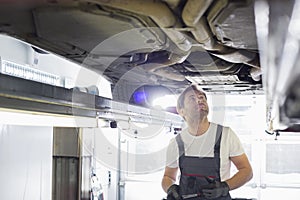 Mid adult male automobile mechanic worker examining car in workshop