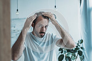 mid adult man with alopecia looking at mirror hair loss