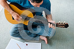 Mid Adult Man Reading Acoustic Guitar Sheet Music In Apartment