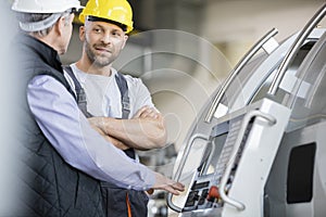 Mid adult manual worker having discussion with colleague by machinery in industry