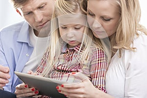 Mid adult parents using tablet PC with daughter at home