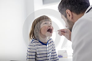 Mid adult pediatrician checking boy patient with depressor at hospital