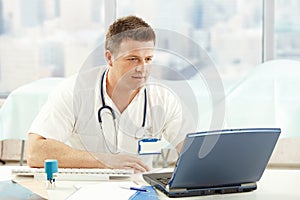 Mid-adult physician working with laptop photo