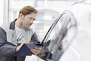 Mid adult repair worker writing on clipboard while examining car in workshop