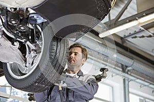 Mid adult technician repairing car's wheel in workshop